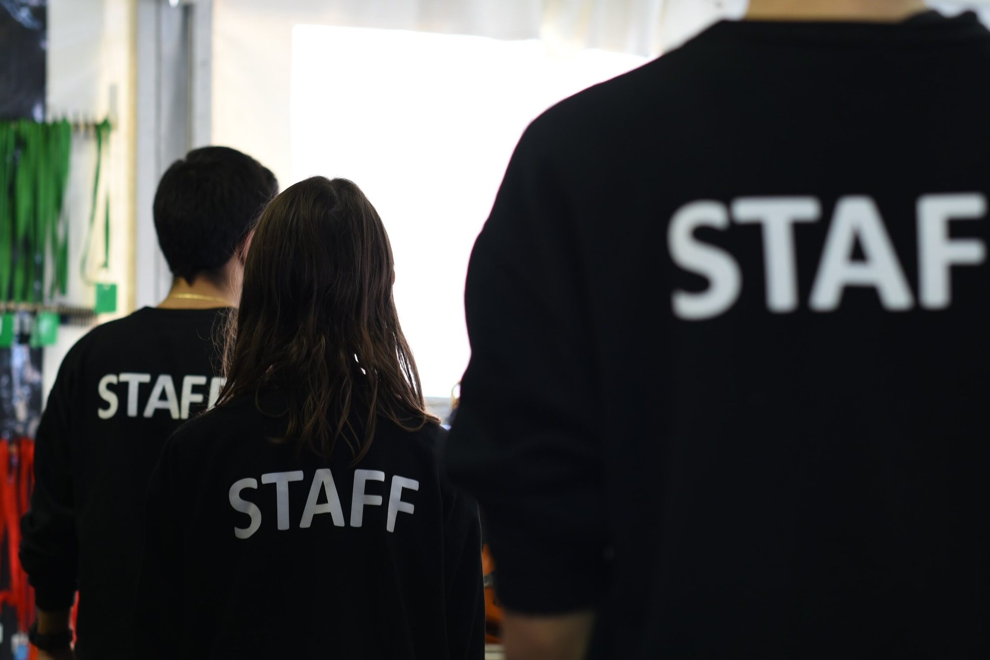 Three people in black T-shirts printed with STAFF, seen from behind