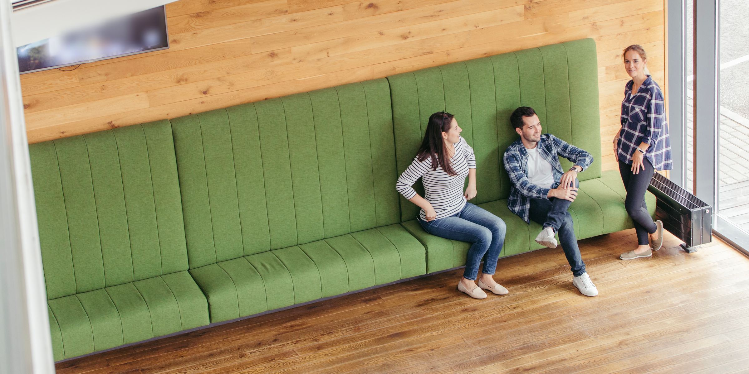 Three people talking on a long bench in a bright waiting area