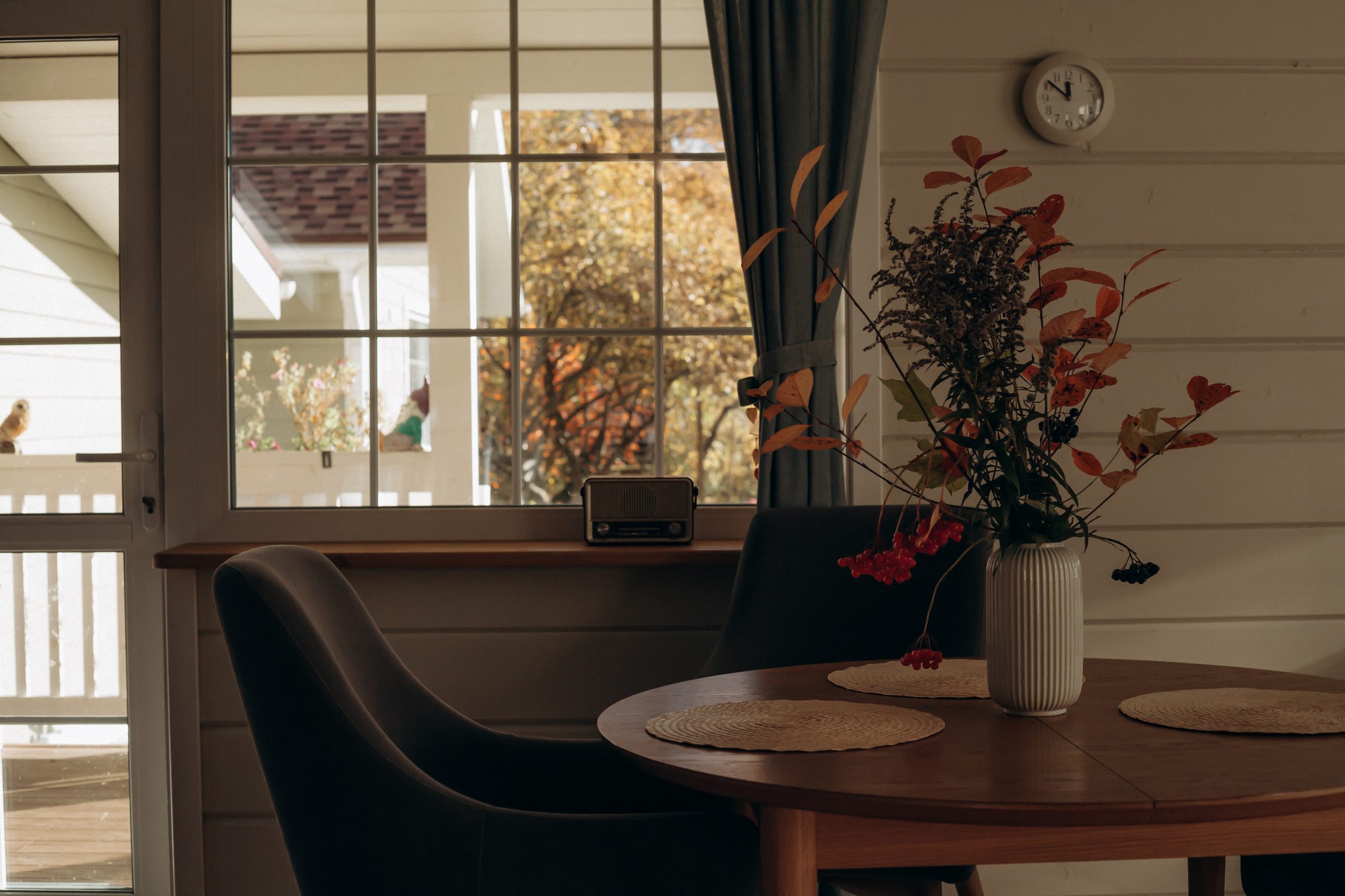 A quiet room: a round table with woven placemats and a chair, and a vase of autumn branches beside a bright window