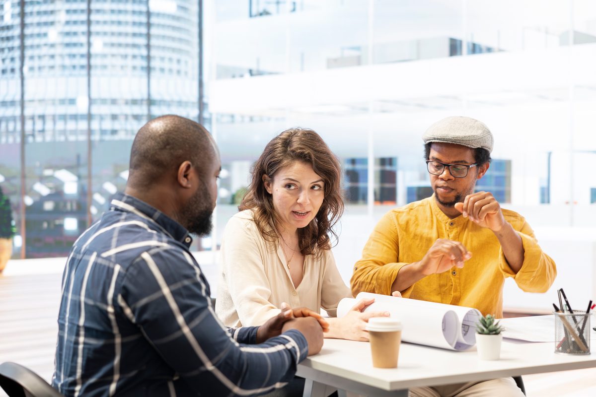 Three people talking over papers at a round table