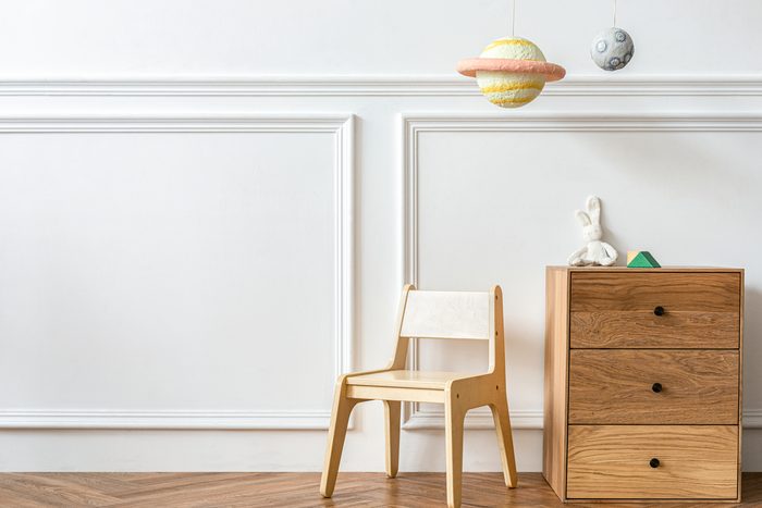 An empty child-sized room: a small wooden chair beside a chest of drawers, with a planet mobile hanging overhead
