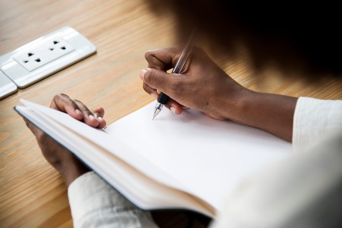 A hand writing with a pen in an open, blank notebook on a wooden desk