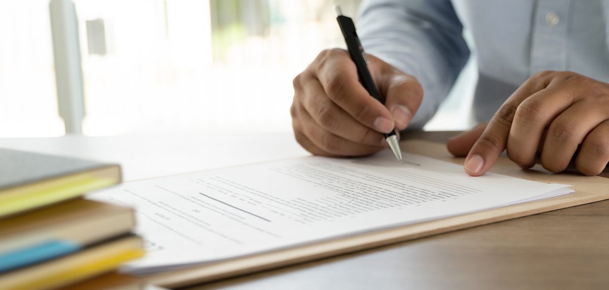 A hand annotating a printed report with a pen, beside a small stack of books