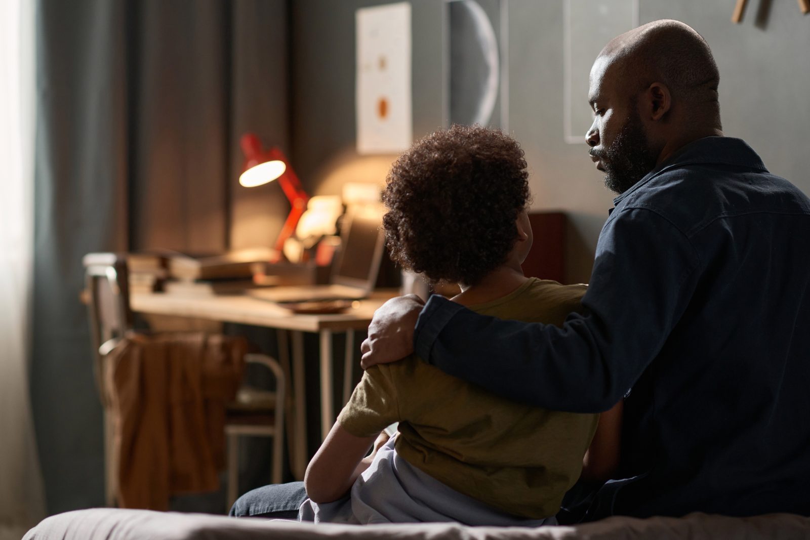 A parent with an arm around their son, seen from behind